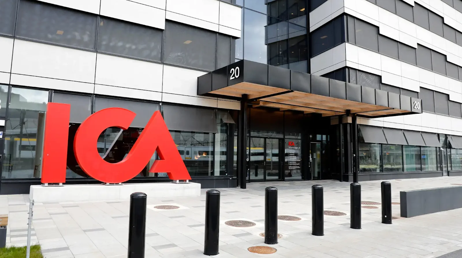 The red ICA logo at the entrance of ICA's headquarters in Solna, Stockholm. A large modern office building with the address 20 above the entrance.